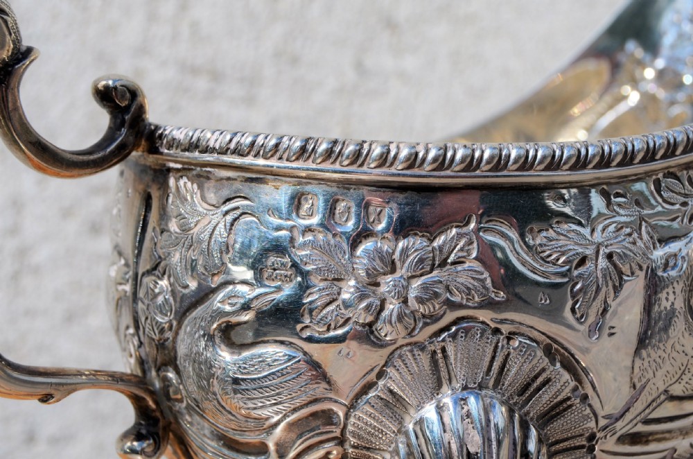 A matching pair of silver sauce boats featuring ornate floral repousse chasing, double-scroll handles, and shell-capped pad feet. View VII