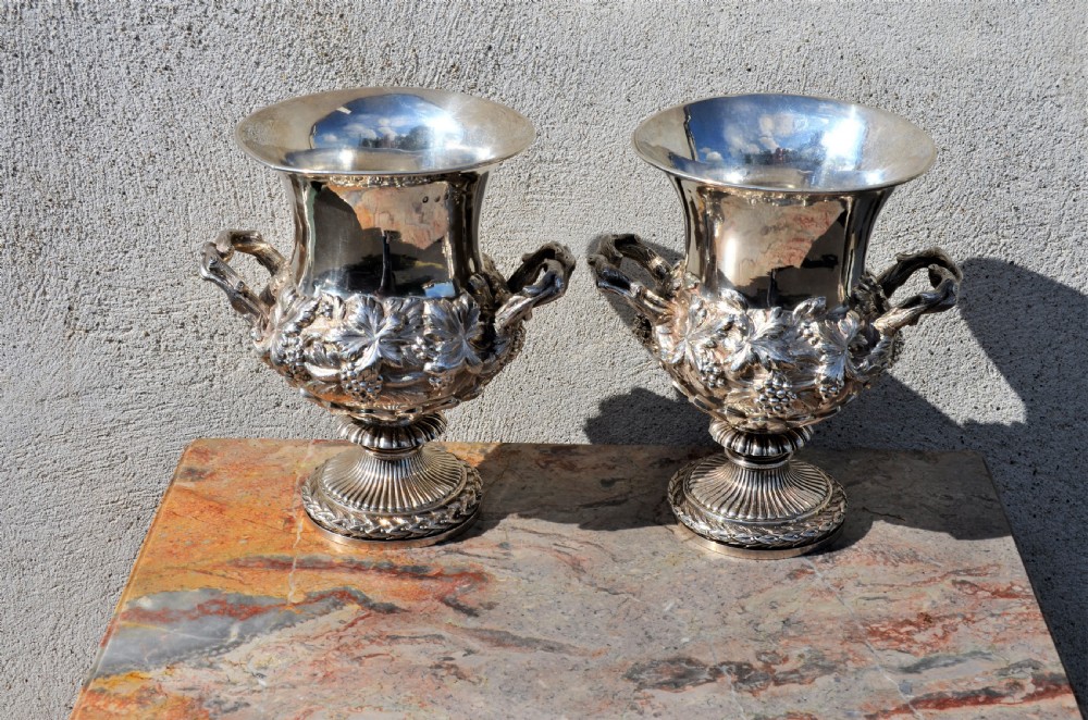 A pair of silver twin-handled urn-shaped vases featuring raised grapevine ornamentation, branch-form handles, and fluted pedestal bases.