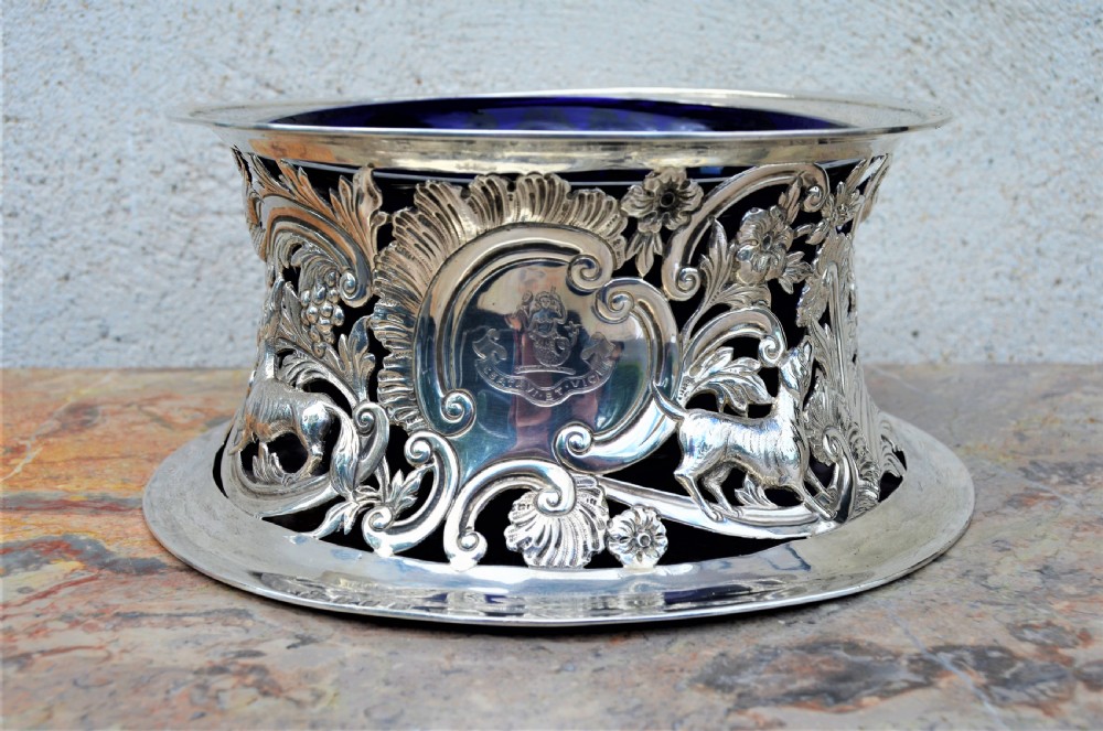 A pierced sterling silver Irish dish ring decorated with repousse animals, scrolls, and an engraved coat of arms, complete with a cobalt blue glass liner.