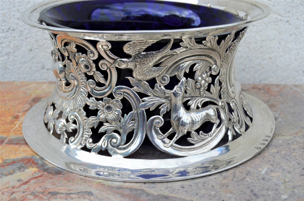 A pierced sterling silver Irish dish ring decorated with repousse animals, scrolls, and an engraved coat of arms, complete with a cobalt blue glass liner. View V