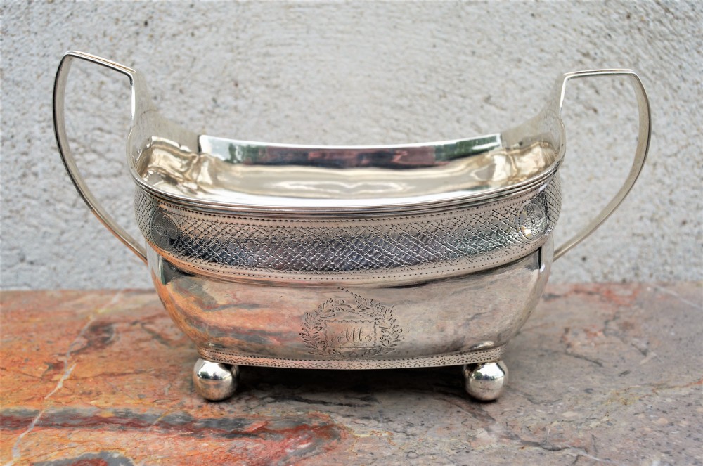 An antique William IV Irish sterling silver basin featuring angular side handles, engraved foliage crest, textured upper band, and ball feet.