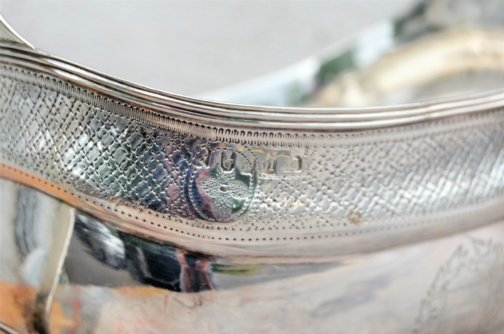 An antique William IV Irish sterling silver basin featuring angular side handles, engraved foliage crest, textured upper band, and ball feet. View II