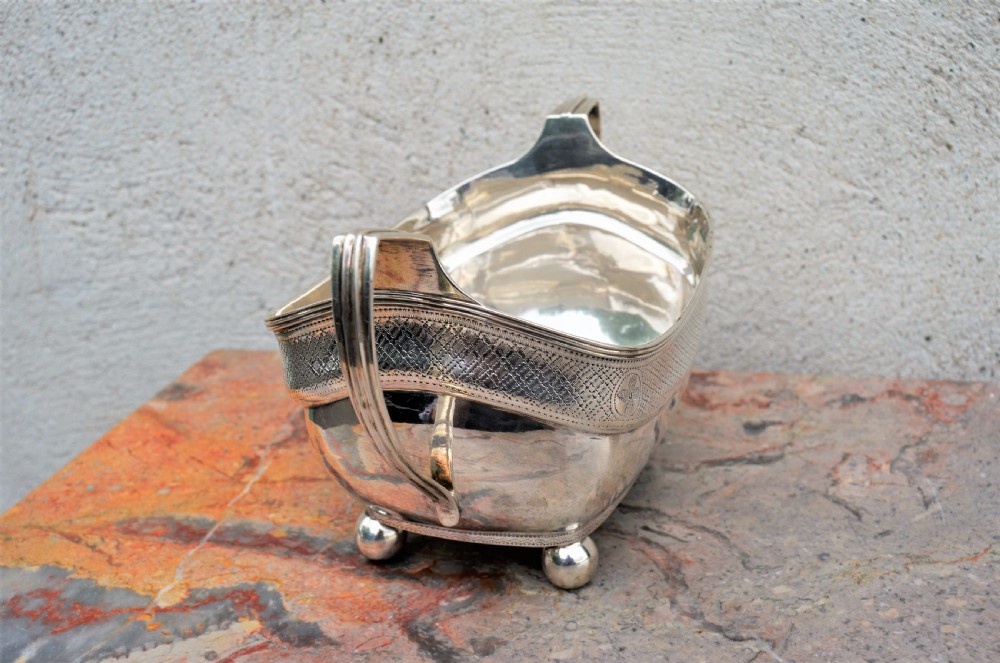 An antique William IV Irish sterling silver basin featuring angular side handles, engraved foliage crest, textured upper band, and ball feet. View IV