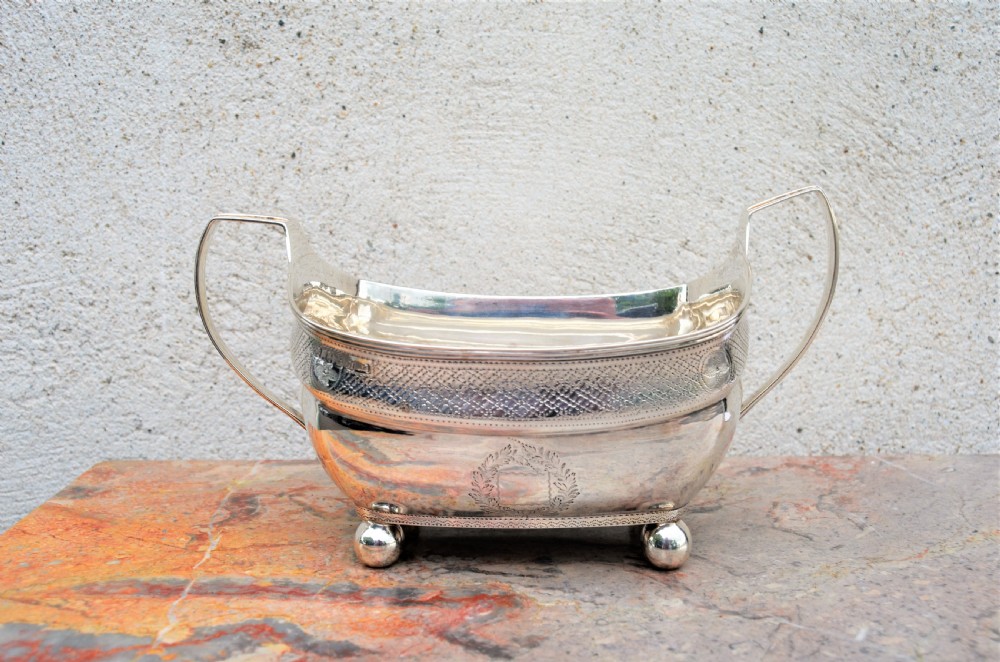 An antique William IV Irish sterling silver basin featuring angular side handles, engraved foliage crest, textured upper band, and ball feet. View V