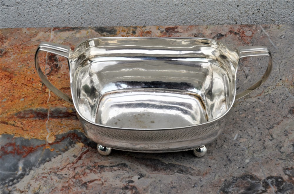 An antique William IV Irish sterling silver basin featuring angular side handles, engraved foliage crest, textured upper band, and ball feet. View VI