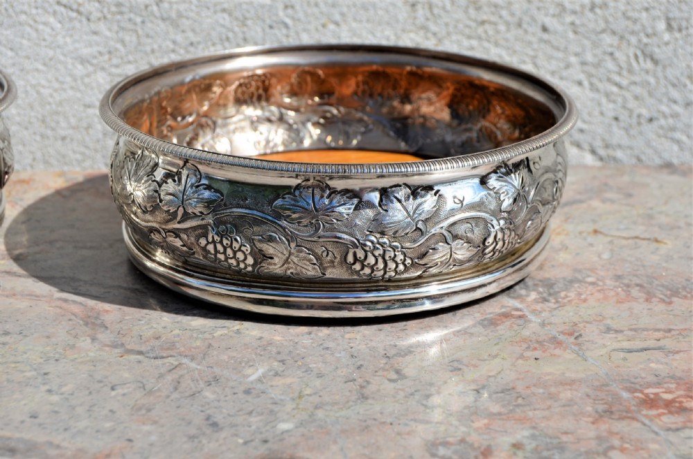 A pair of circular silver wine coasters featuring embossed botanical repousse patterns and turned wooden bases. View II