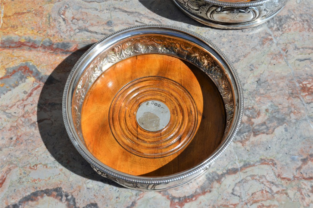 A pair of circular silver wine coasters featuring embossed botanical repousse patterns and turned wooden bases. View III