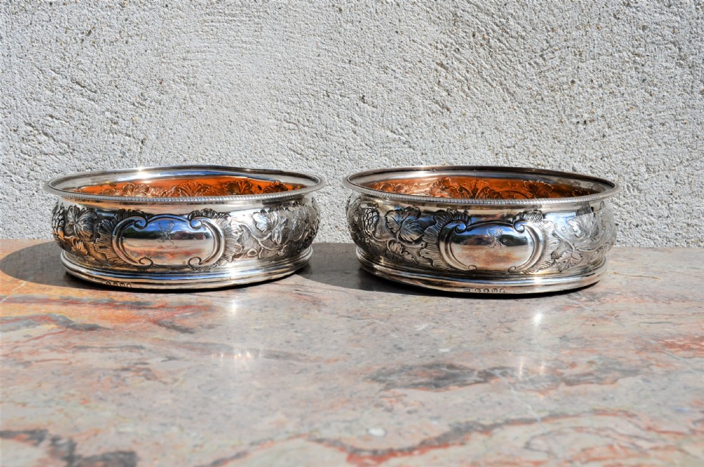 A pair of circular silver wine coasters featuring embossed botanical repousse patterns and turned wooden bases. View IV