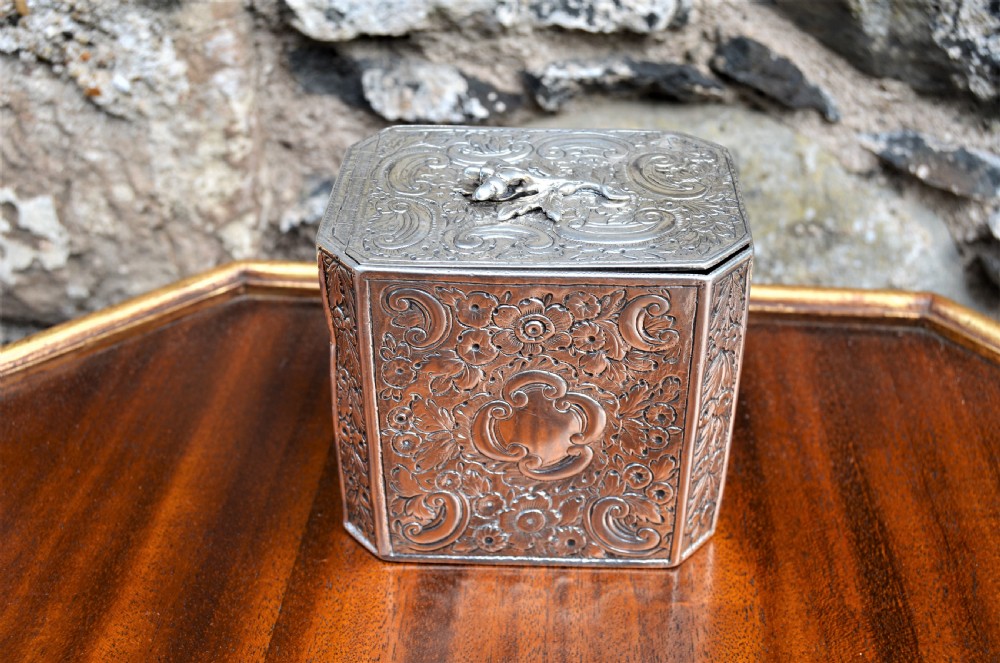 An octagonal Georgian sterling silver tea caddy decorated with intricate floral repousse patterns and featuring a keyhole on the front panel. View II