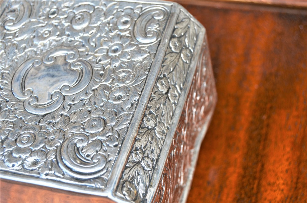 An octagonal Georgian sterling silver tea caddy decorated with intricate floral repousse patterns and featuring a keyhole on the front panel. View III
