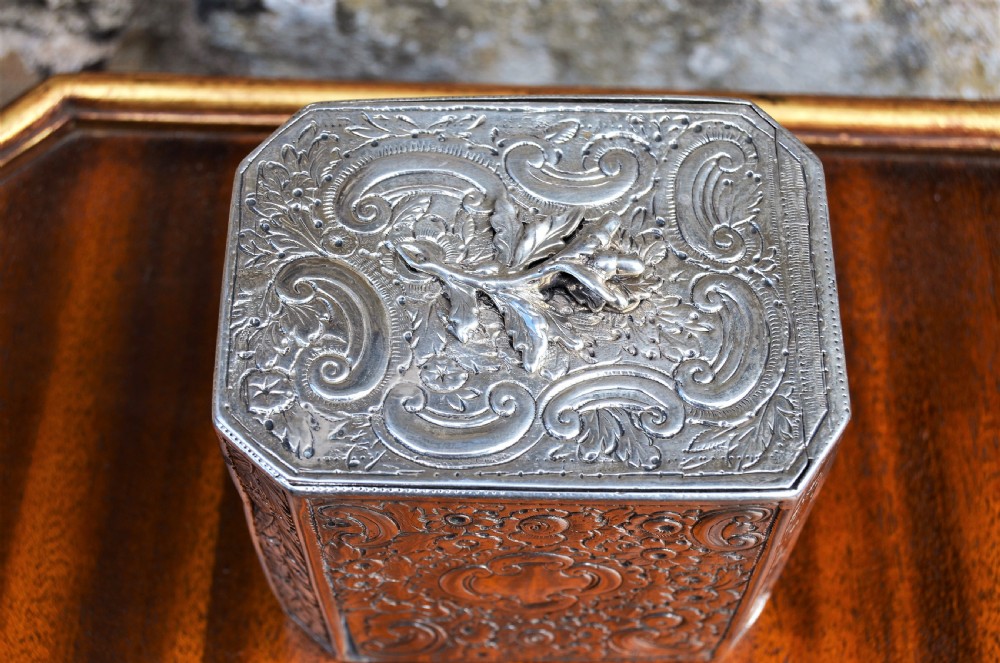 An octagonal Georgian sterling silver tea caddy decorated with intricate floral repousse patterns and featuring a keyhole on the front panel. View V