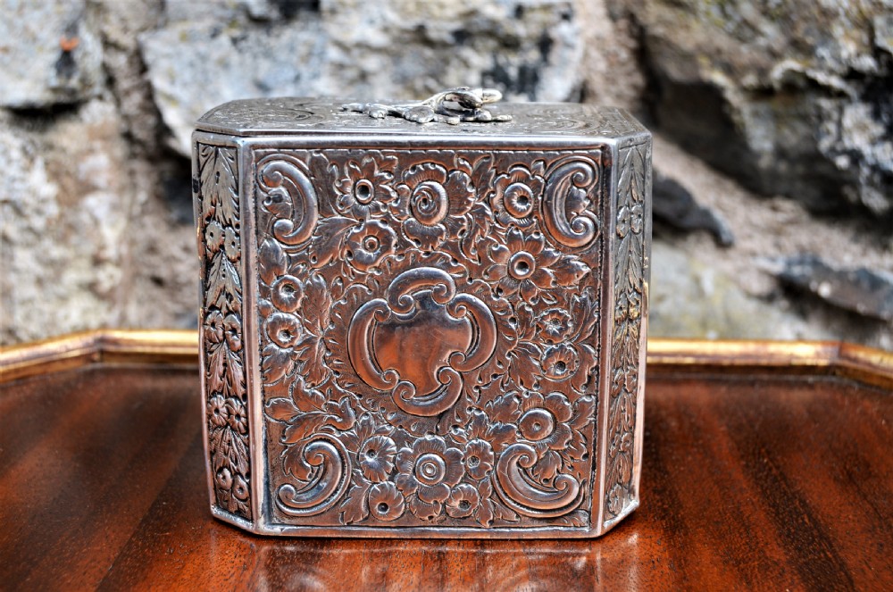 An octagonal Georgian sterling silver tea caddy decorated with intricate floral repousse patterns and featuring a keyhole on the front panel. View VI