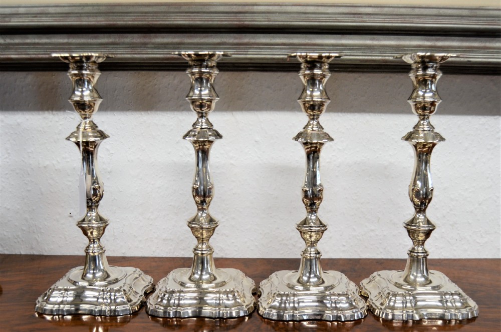 A set of four matching silver candlesticks featuring baluster-shaped stems and moulded square bases arranged side-by-side.