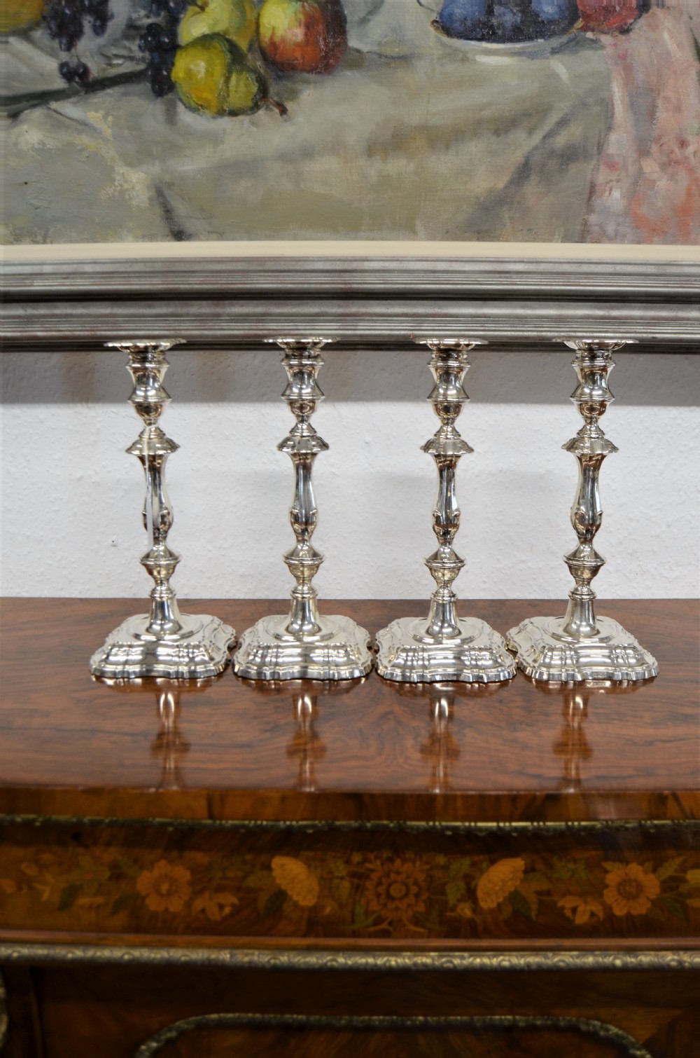 A set of four matching silver candlesticks featuring baluster-shaped stems and moulded square bases arranged side-by-side. View V