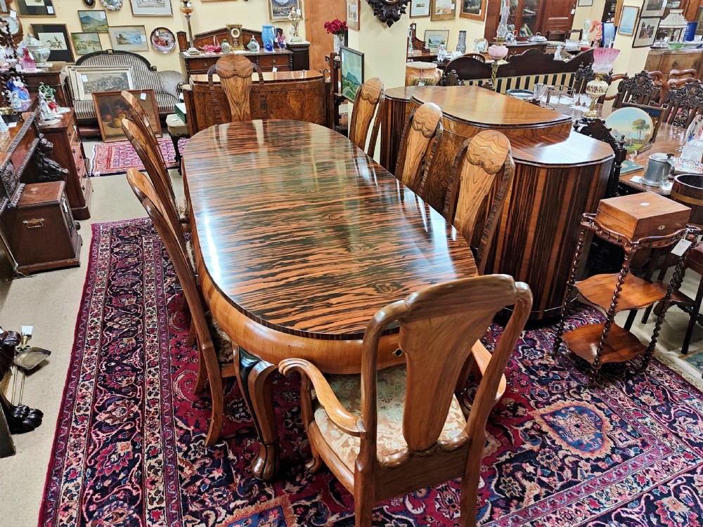 A French Art Deco eleven-piece dining suite comprising an oval dining table, matching high-back chairs, and sideboards featuring heavily figured calamander and macassar ebony veneers.