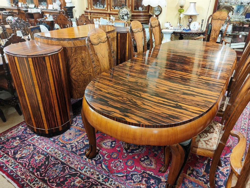 A French Art Deco eleven-piece dining suite comprising an oval dining table, matching high-back chairs, and sideboards featuring heavily figured calamander and macassar ebony veneers. View IX