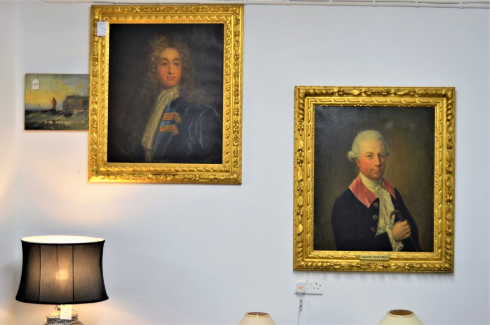 A pair of 19th-century oil portraits depicting male subjects in elaborate attire, enclosed within ornate, heavily carved gilt frames.