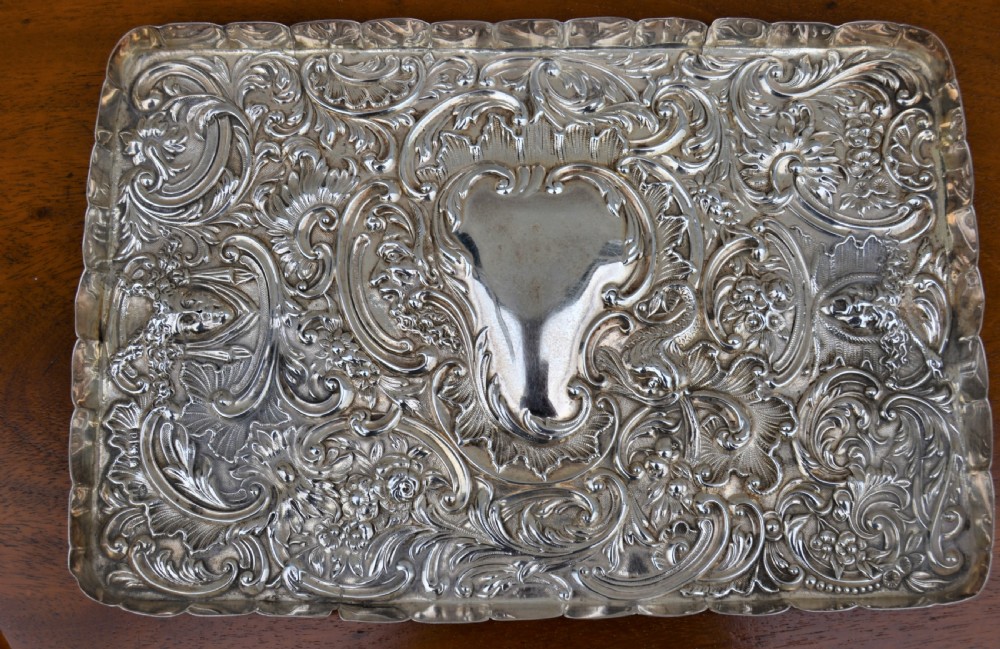 A rectangular sterling silver dressing table tray featuring detailed repousse scrollwork, foliate patterns, and a smooth central cartouche.
