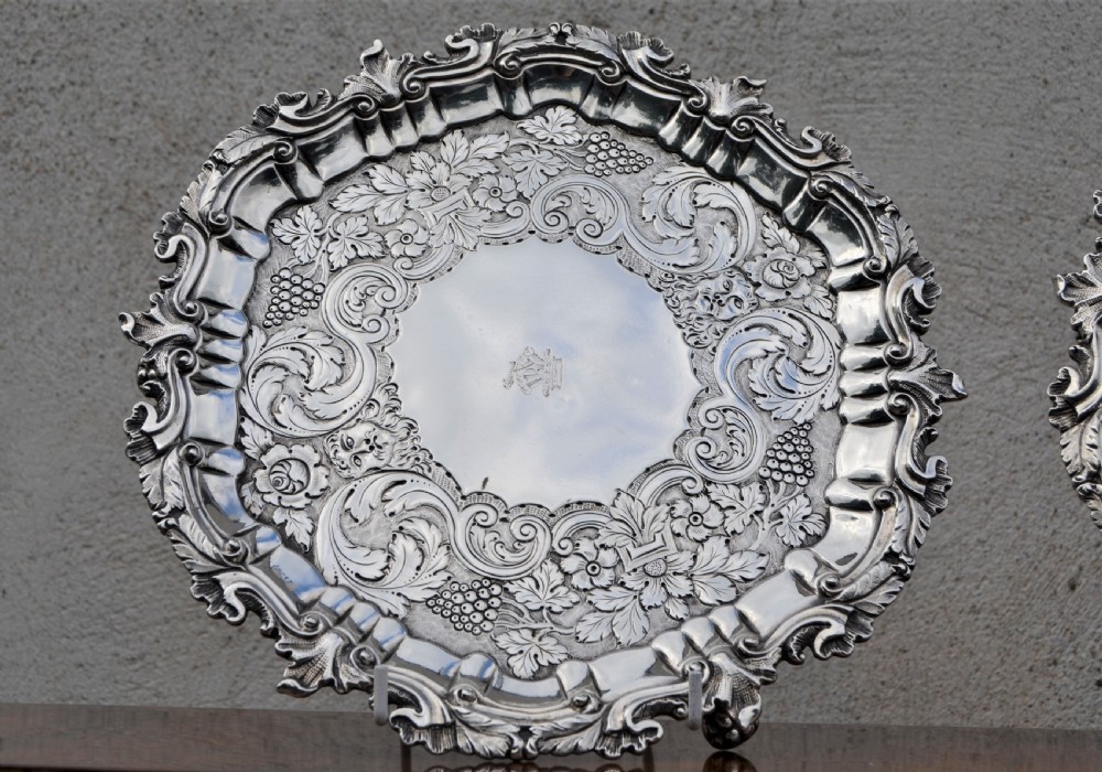 A pair of circular sterling silver salvers featuring intricate chased foliate and grapevine borders surrounding a central polished field. View II