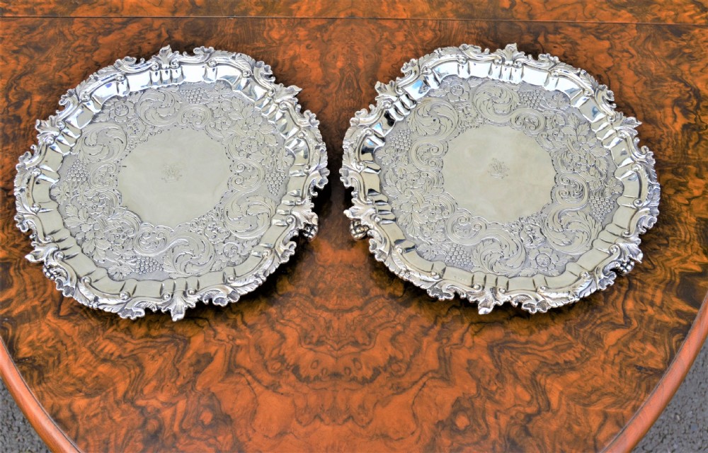 A pair of circular sterling silver salvers featuring intricate chased foliate and grapevine borders surrounding a central polished field. View VII