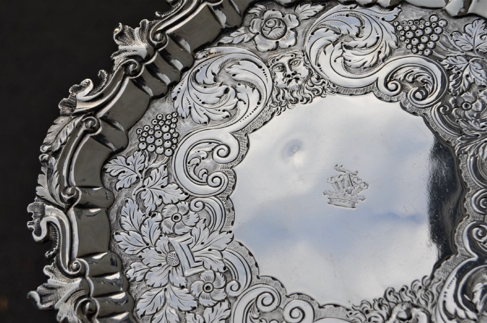 A pair of circular sterling silver salvers featuring intricate chased foliate and grapevine borders surrounding a central polished field. View VIII