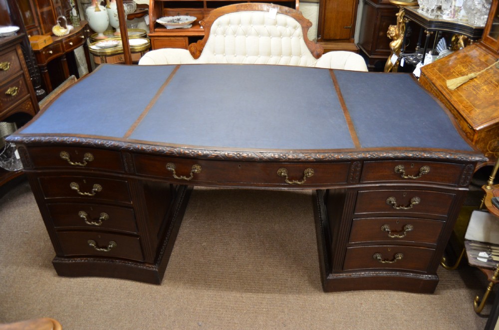 A large mahogany partners desk featuring a three-panel blue leather writing surface, carved edge detailing, brass handles, and twin pedestals with drawers.