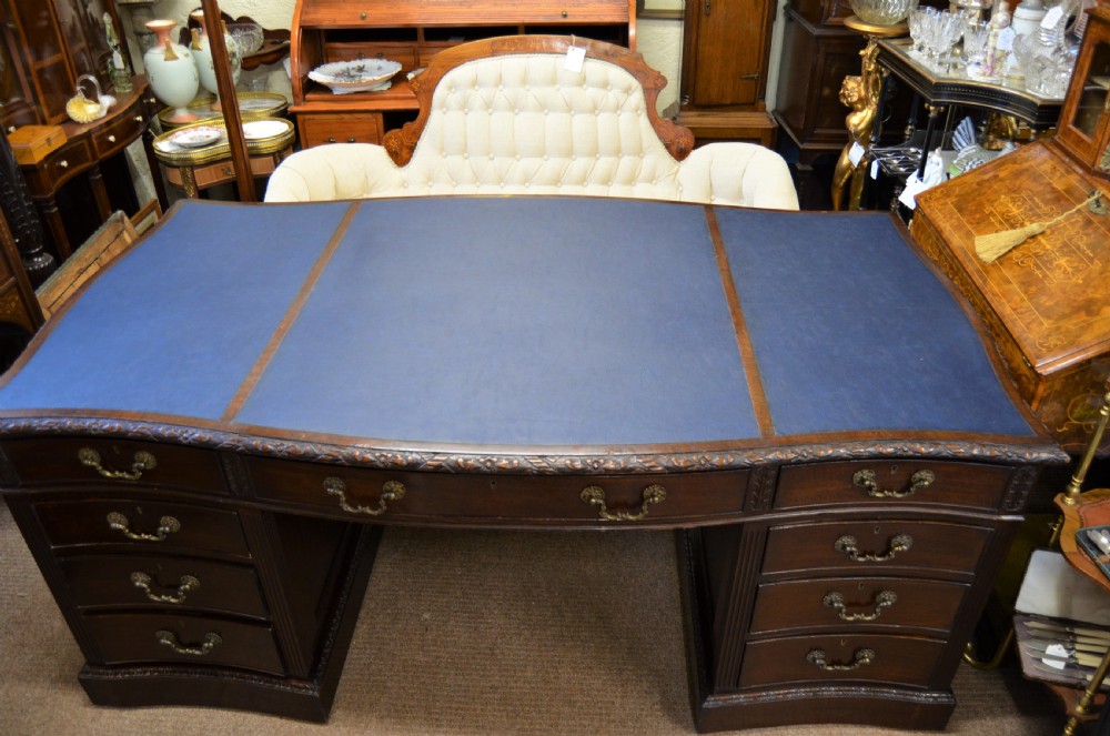 A large mahogany partners desk featuring a three-panel blue leather writing surface, carved edge detailing, brass handles, and twin pedestals with drawers. View II