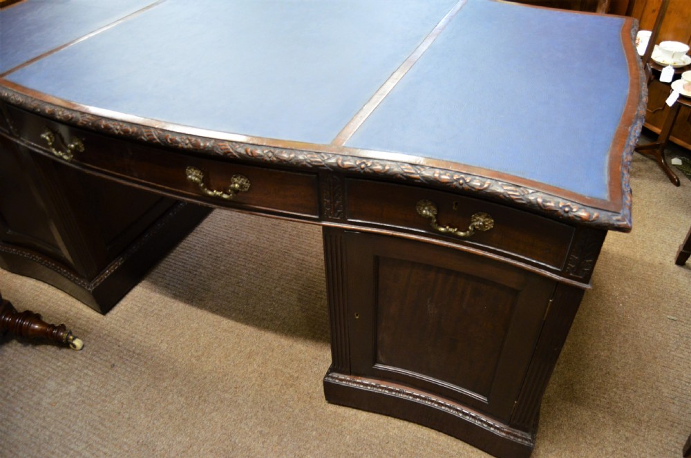 A large mahogany partners desk featuring a three-panel blue leather writing surface, carved edge detailing, brass handles, and twin pedestals with drawers. View III