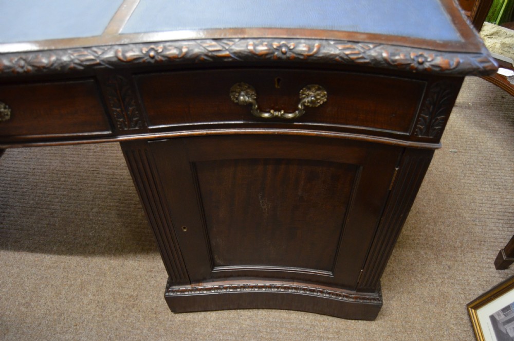 A large mahogany partners desk featuring a three-panel blue leather writing surface, carved edge detailing, brass handles, and twin pedestals with drawers. View IV