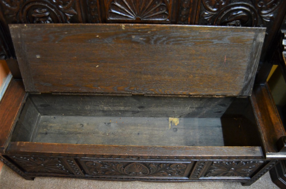 A dark Victorian carved oak monks bench with a relief-carved backrest displaying portrait medallions and foliage above a hinged box seat. View IV