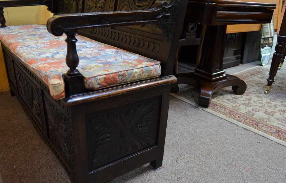 A dark Victorian carved oak monks bench with a relief-carved backrest displaying portrait medallions and foliage above a hinged box seat. View V