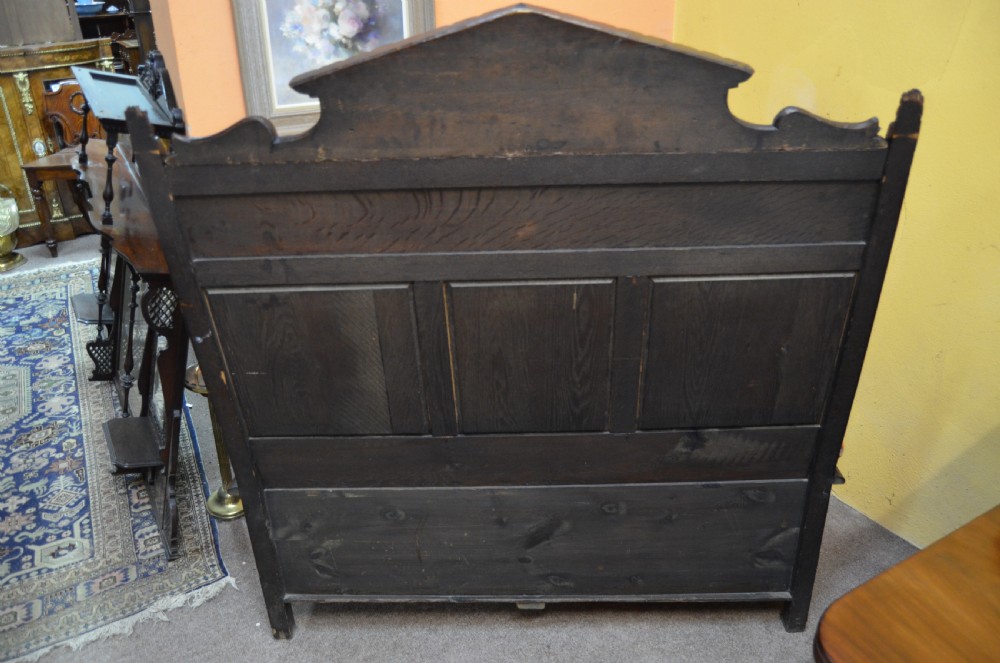 A dark Victorian carved oak monks bench with a relief-carved backrest displaying portrait medallions and foliage above a hinged box seat. View VI