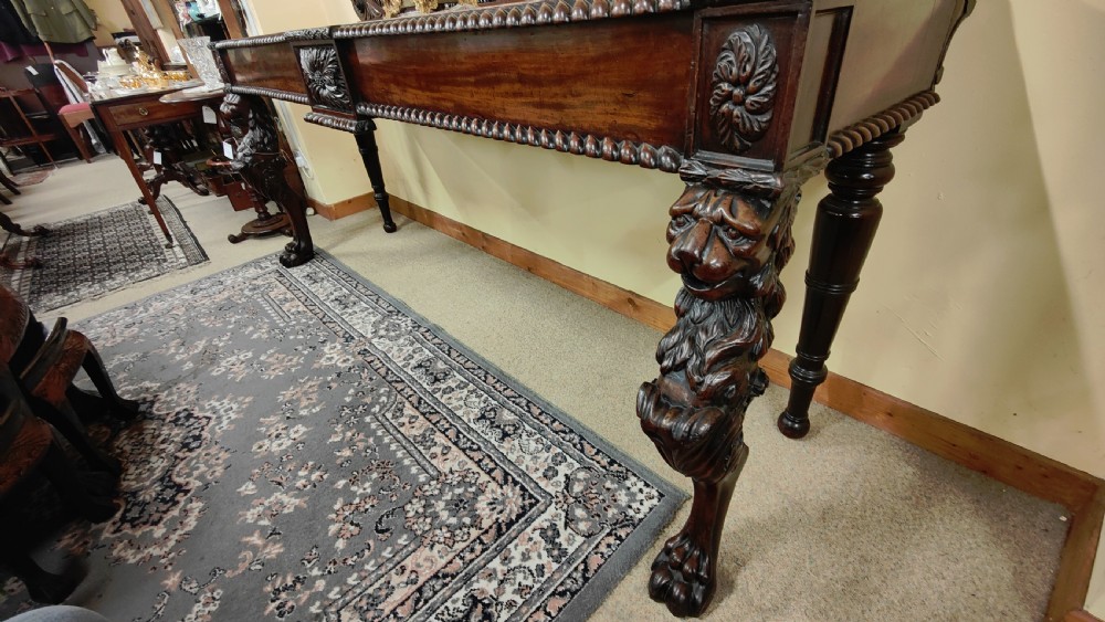 A William IV carved mahogany serving table featuring a raised carved backboard, rope-twist edging, central carved motif, and front legs with carved lion monopodia. View V