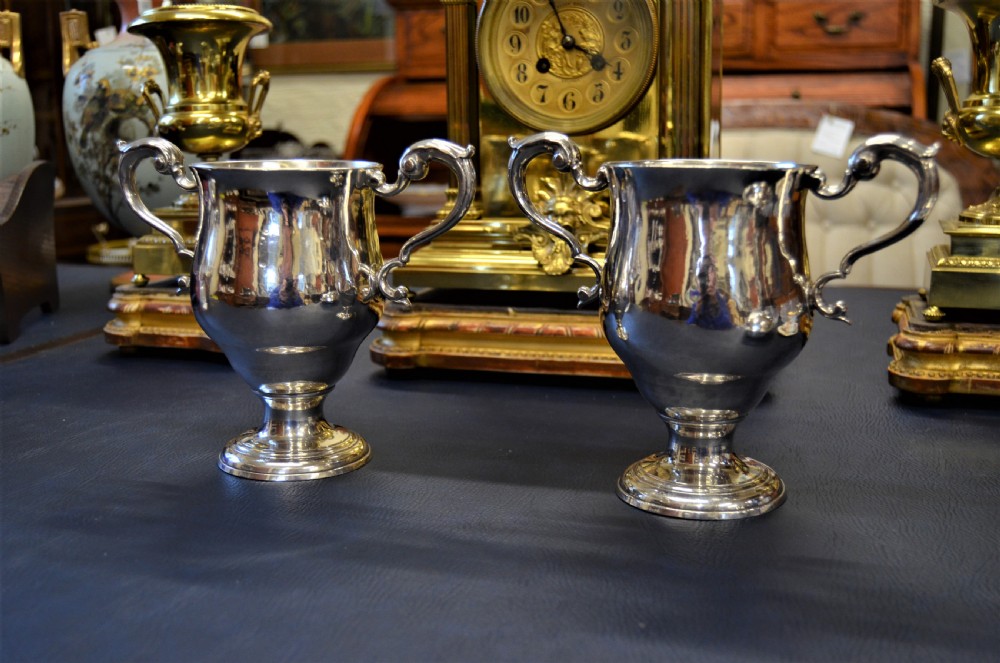 A pair of antique 18th-century silver two-handled cups with scroll handles, crest engravings, and turned pedestal bases. View II