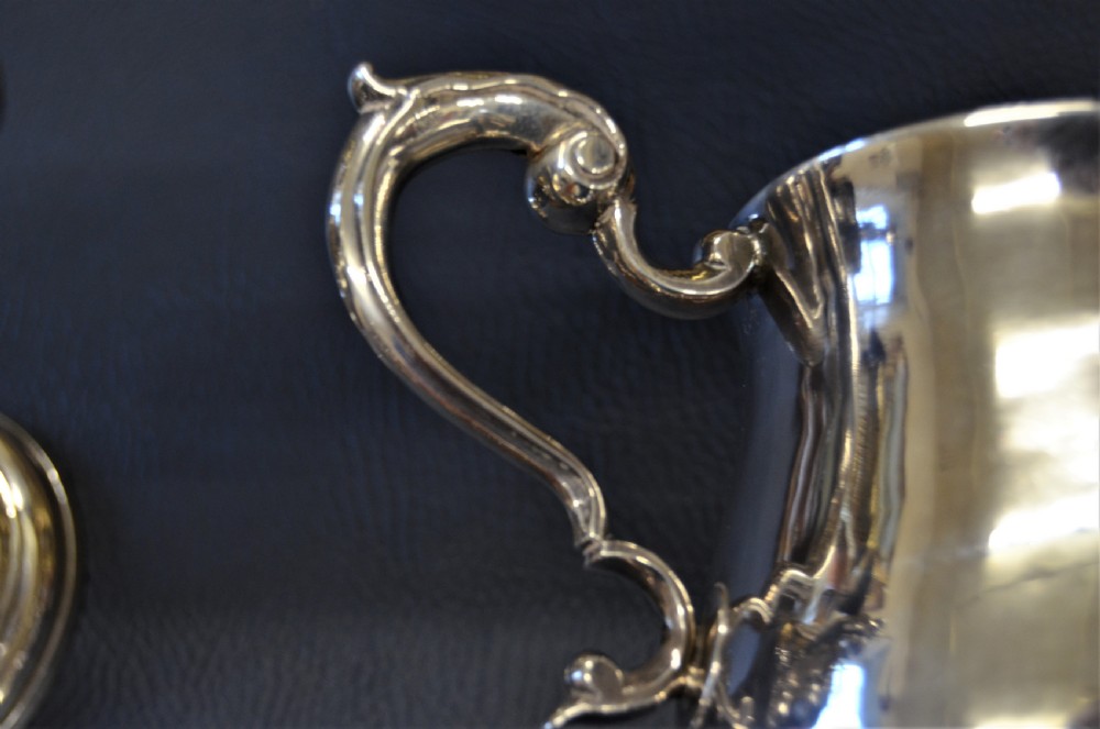 A pair of antique 18th-century silver two-handled cups with scroll handles, crest engravings, and turned pedestal bases. View III