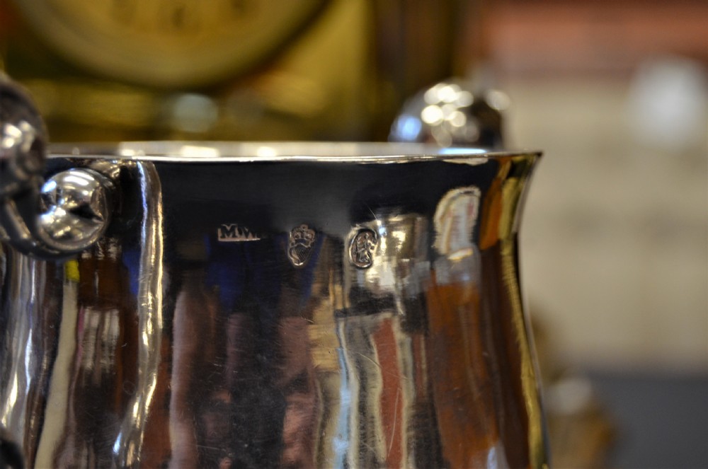 A pair of antique 18th-century silver two-handled cups with scroll handles, crest engravings, and turned pedestal bases. View V