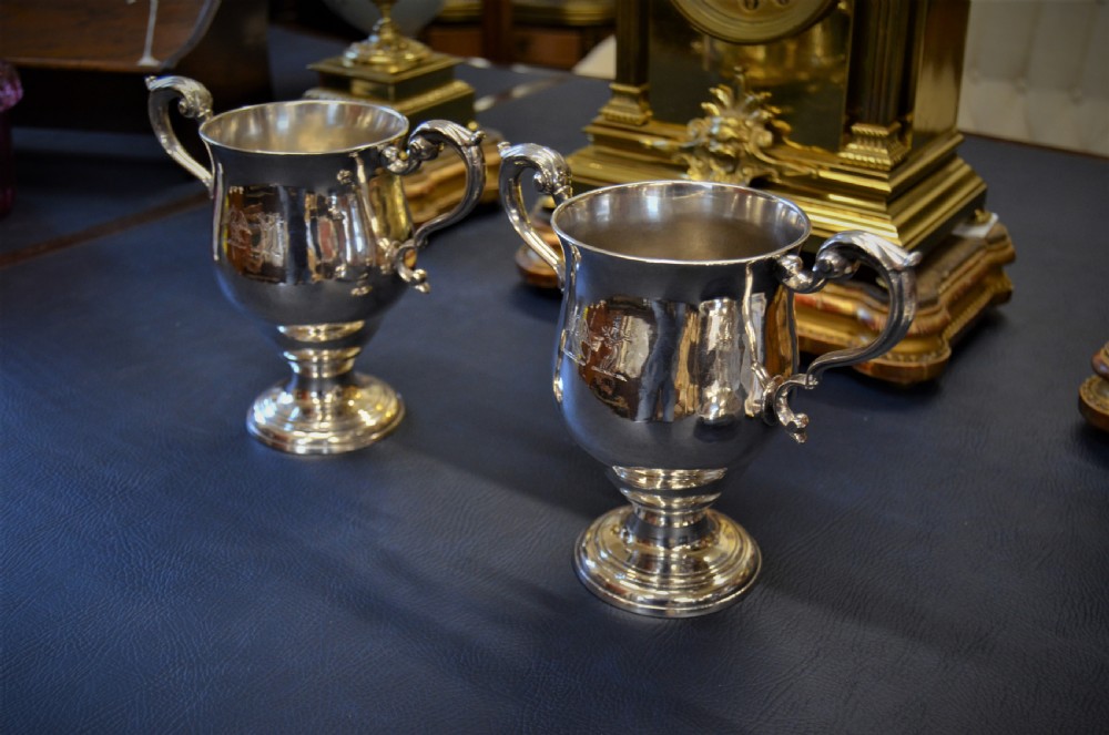 A pair of antique 18th-century silver two-handled cups with scroll handles, crest engravings, and turned pedestal bases. View VI