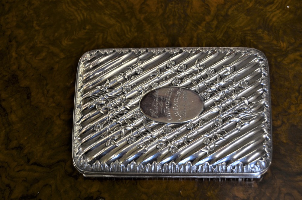 A rectangular Edwardian sterling silver cigarette case featuring diagonal fluting, chased floral motifs, and a central engraved oval cartouche.