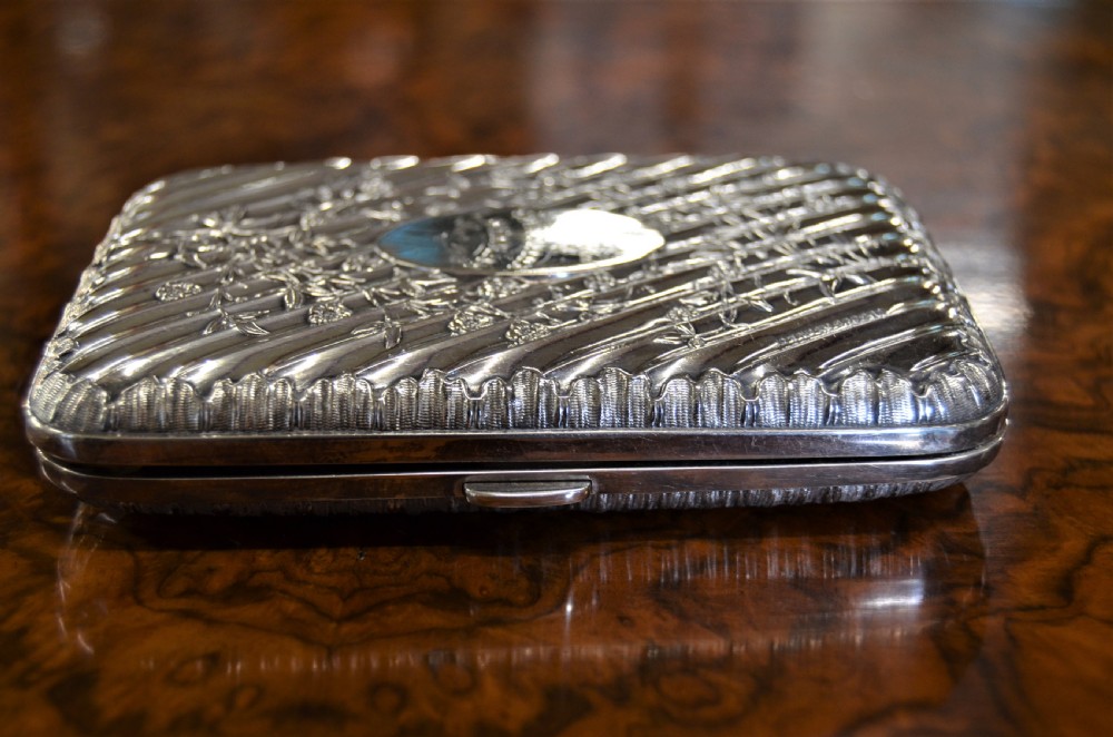 A rectangular Edwardian sterling silver cigarette case featuring diagonal fluting, chased floral motifs, and a central engraved oval cartouche. View II