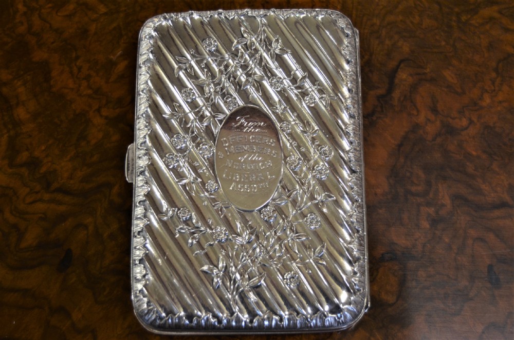 A rectangular Edwardian sterling silver cigarette case featuring diagonal fluting, chased floral motifs, and a central engraved oval cartouche. View IV