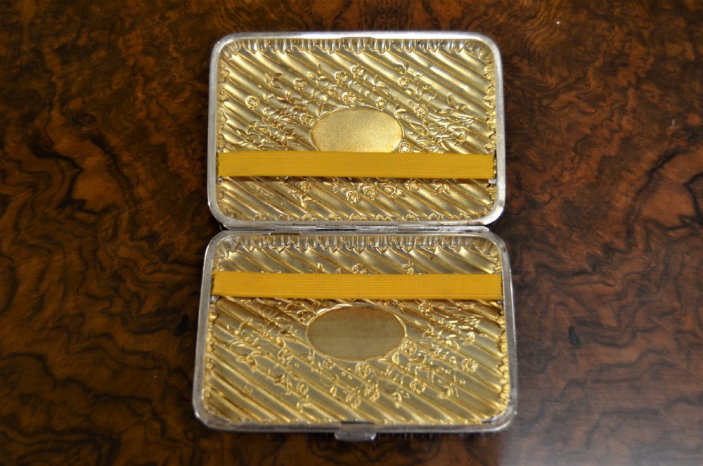A rectangular Edwardian sterling silver cigarette case featuring diagonal fluting, chased floral motifs, and a central engraved oval cartouche. View V