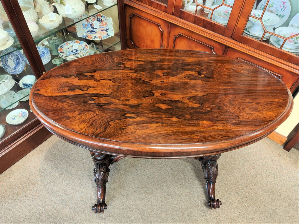 An antique Victorian oval rosewood centre table featuring a highly figured veneer top supported by carved trestle legs and a decorative stretcher. View II