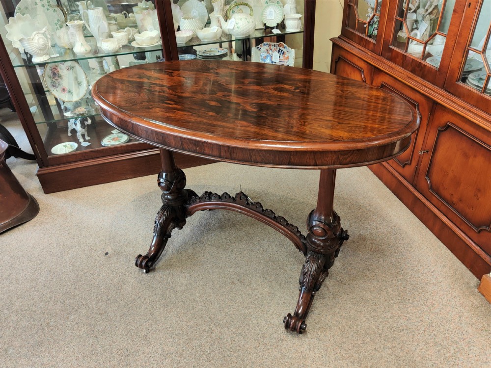 An antique Victorian oval rosewood centre table featuring a highly figured veneer top supported by carved trestle legs and a decorative stretcher. View III