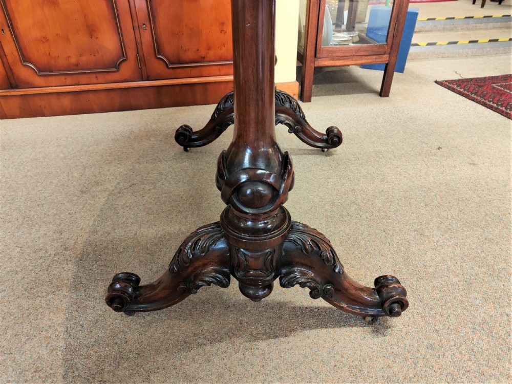An antique Victorian oval rosewood centre table featuring a highly figured veneer top supported by carved trestle legs and a decorative stretcher. View IV