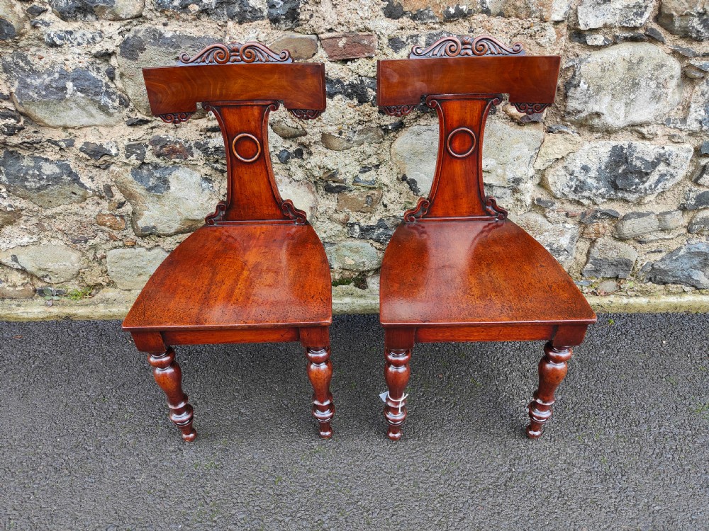 A pair of 19th-century rich brown mahogany hall chairs with carved backrests, solid seats, and turned front legs. View VI