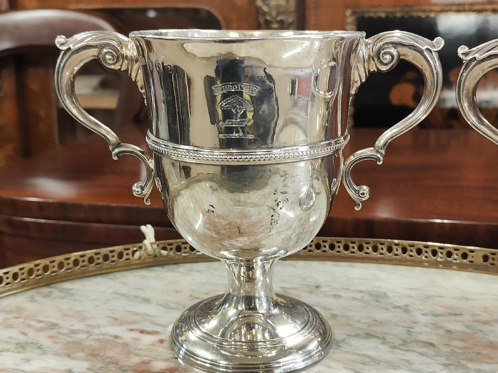A pair of 18th-century Irish sterling silver twin-handled cups featuring central ribbed girdles and engraved crests on pedestal bases. View III
