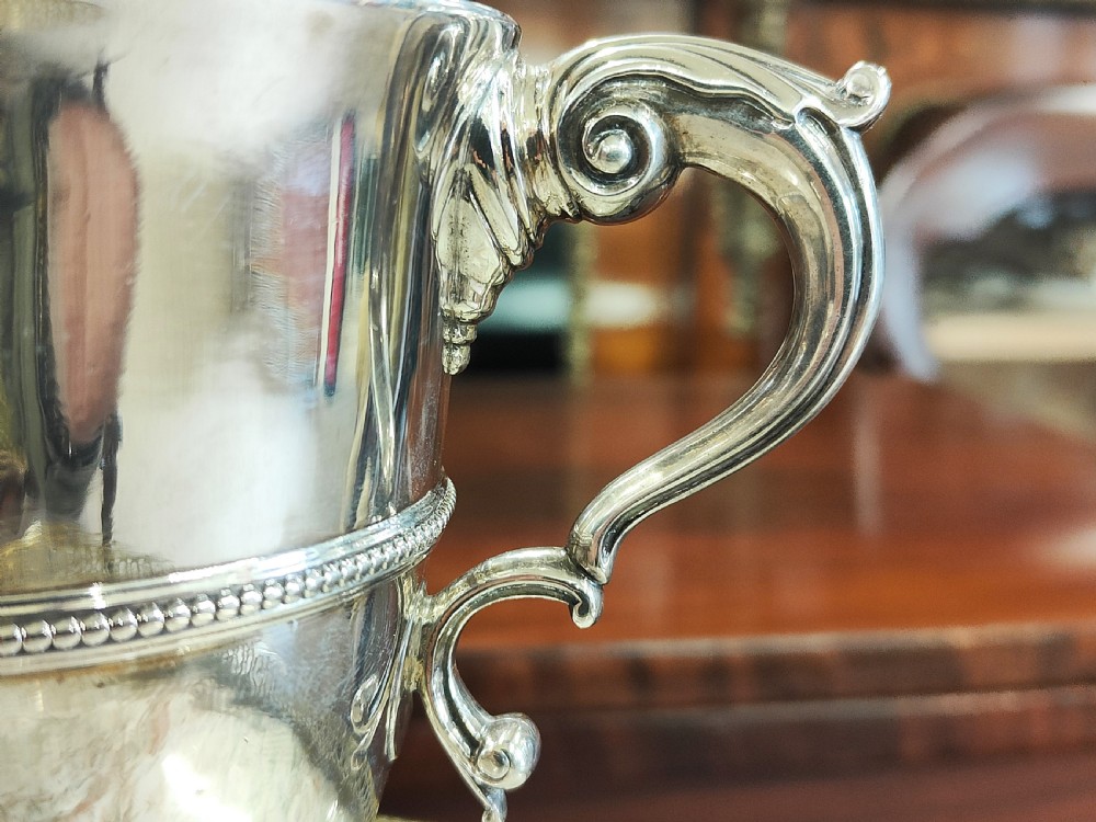 A pair of 18th-century Irish sterling silver twin-handled cups featuring central ribbed girdles and engraved crests on pedestal bases. View IV