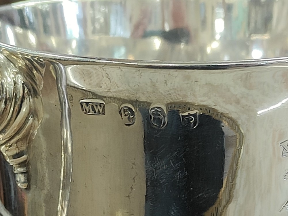 A pair of 18th-century Irish sterling silver twin-handled cups featuring central ribbed girdles and engraved crests on pedestal bases. View V