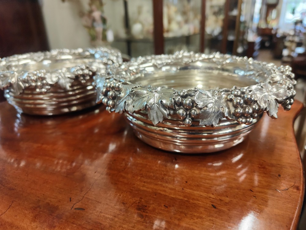 A pair of circular Georgian silver wine coasters featuring intricate cast grape and vine leaf borders with turned wooden bases. View III