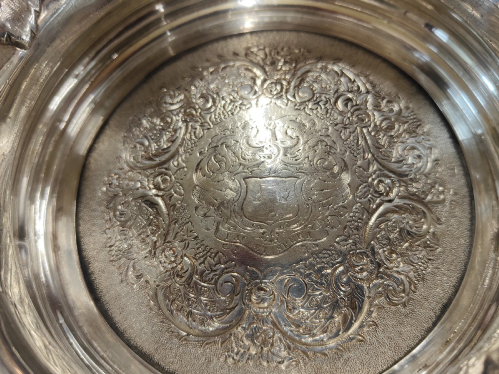 A pair of circular Georgian silver wine coasters featuring intricate cast grape and vine leaf borders with turned wooden bases. View V